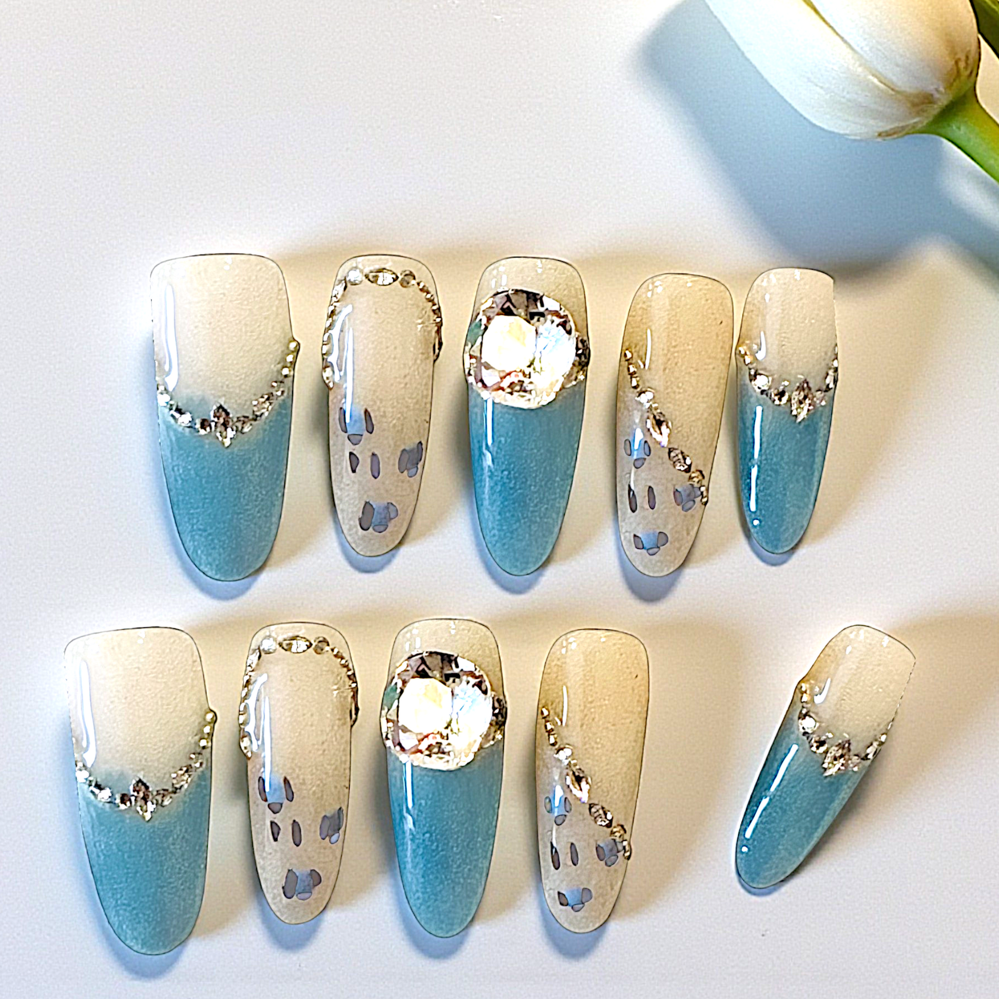 Set of decorative nails with blue and beige gradient and rhinestone accents on a white background.
