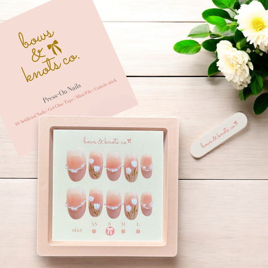 Press-on nails set with a pink box and floral design on a wooden surface.