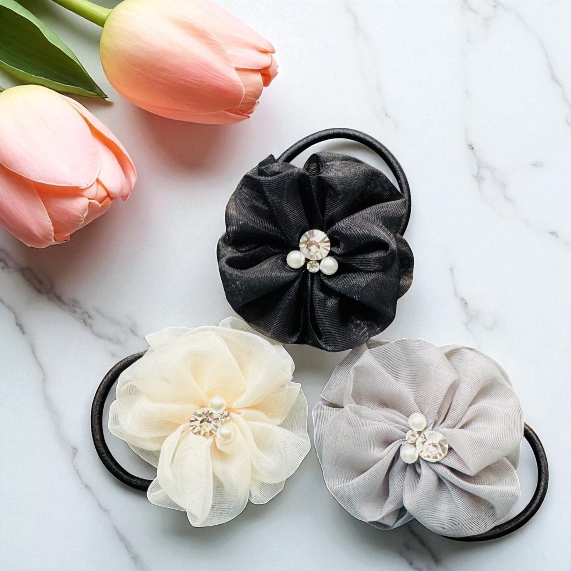 Three fabric hair ties with floral designs on a marble surface with tulips.