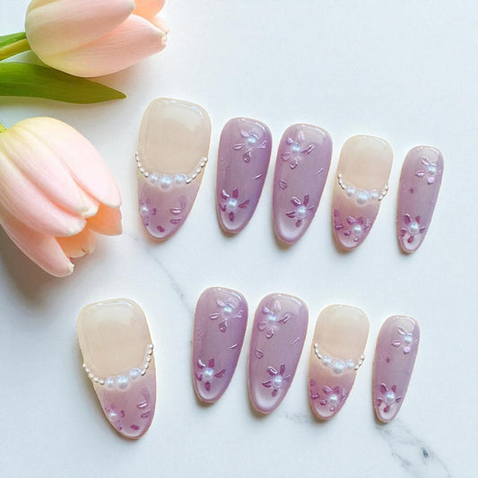 Set of pink and beige gradient nails with floral designs on a marble surface with tulips.