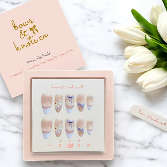 Press-on nails set with a pink box and white tulips on a marble surface