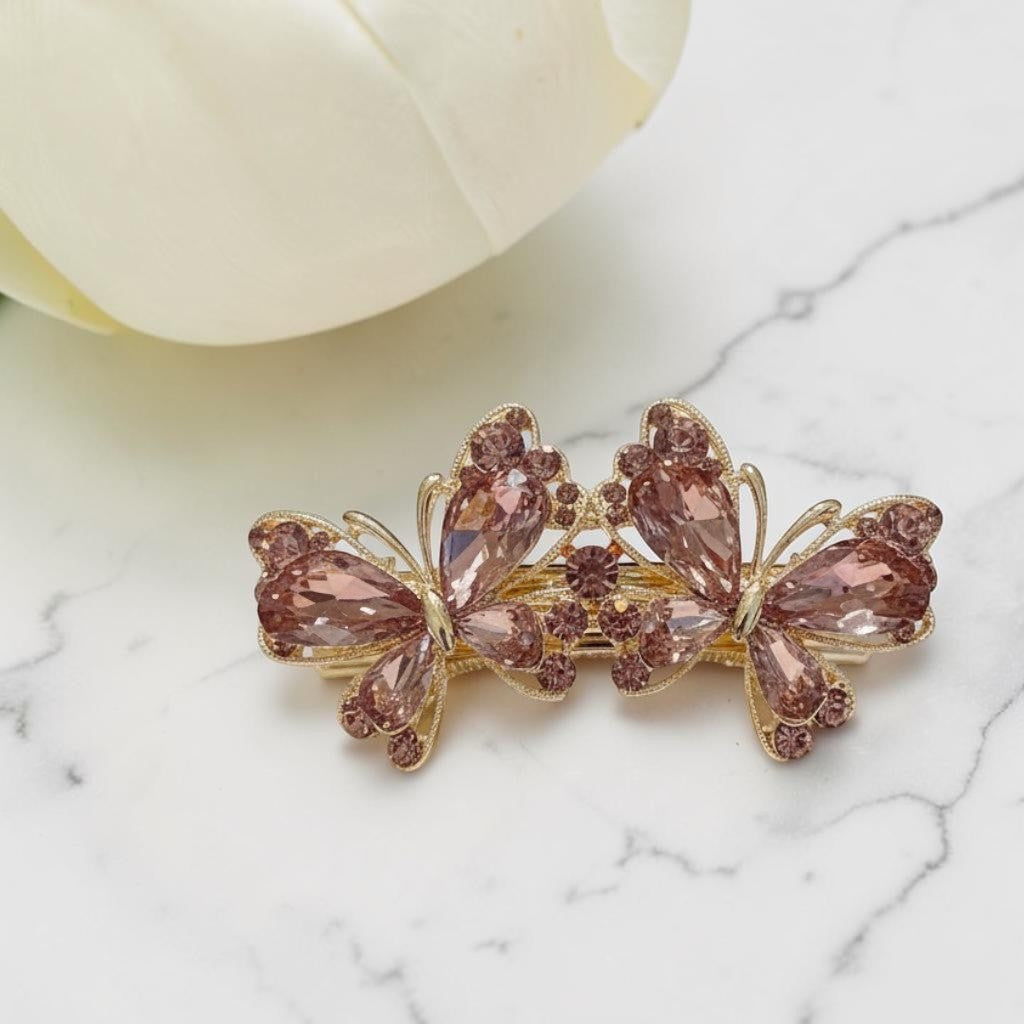 Butterfly-shaped hair clip with pink crystals on a marble surface