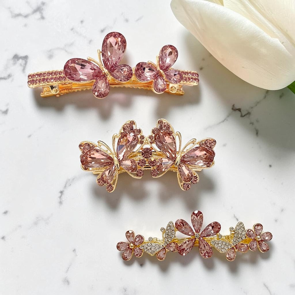 Three decorative hair clips with pink gemstones on a marble surface.