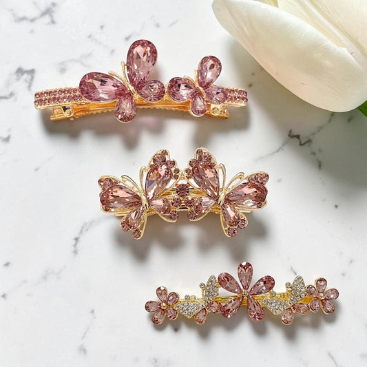 Three decorative hair clips with pink gemstones on a marble surface.