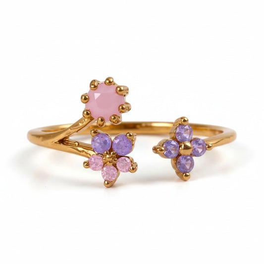 A gold ring featuring a branch design with a pink flower and two purple flower clusters, set against a plain white background.