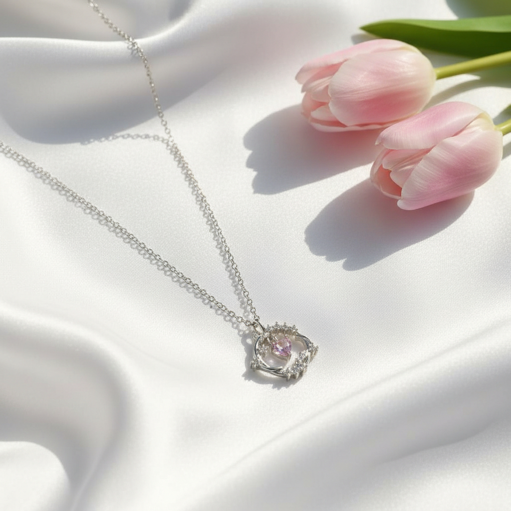 Silver necklace with a pink gemstone pendant on a white fabric background with pink tulips.
