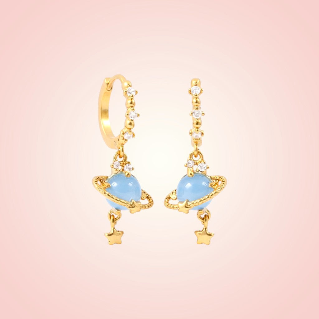Gold earrings with blue heart-shaped stones on a pink background