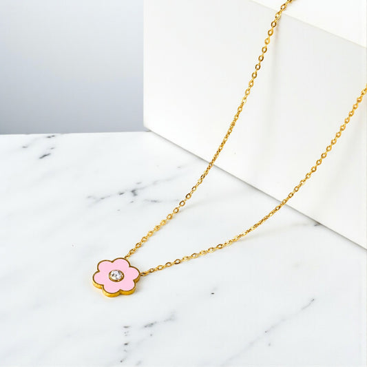 Gold necklace with a pink flower pendant on a marble surface