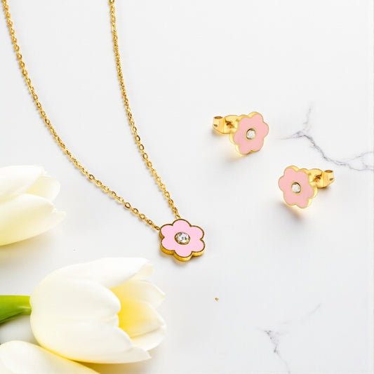 Flower-shaped gold necklace and earrings on a marble surface with white flowers.