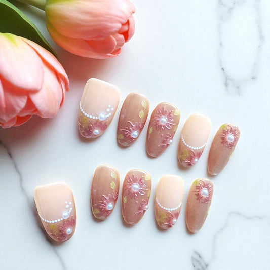 Decorative false nails with floral and pearl details on a marble surface with tulips.