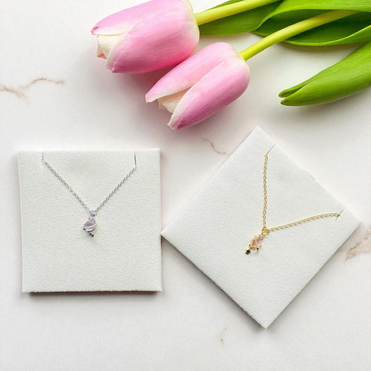 Two necklaces in display boxes with pink tulips on a marble surface