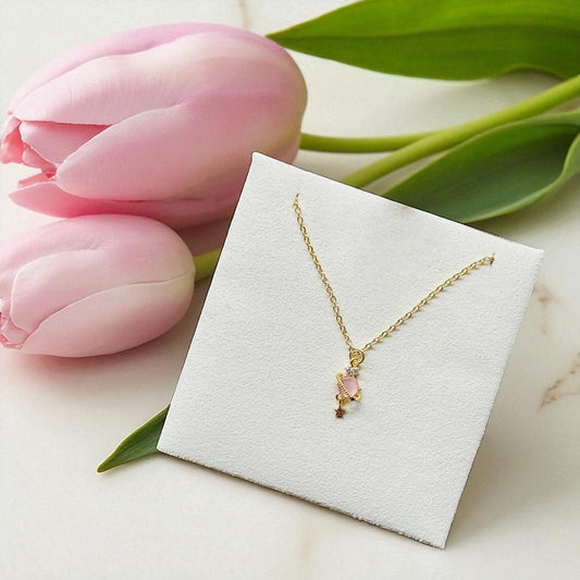 Gold necklace with a pink pendant on a white card, surrounded by pink tulips.
