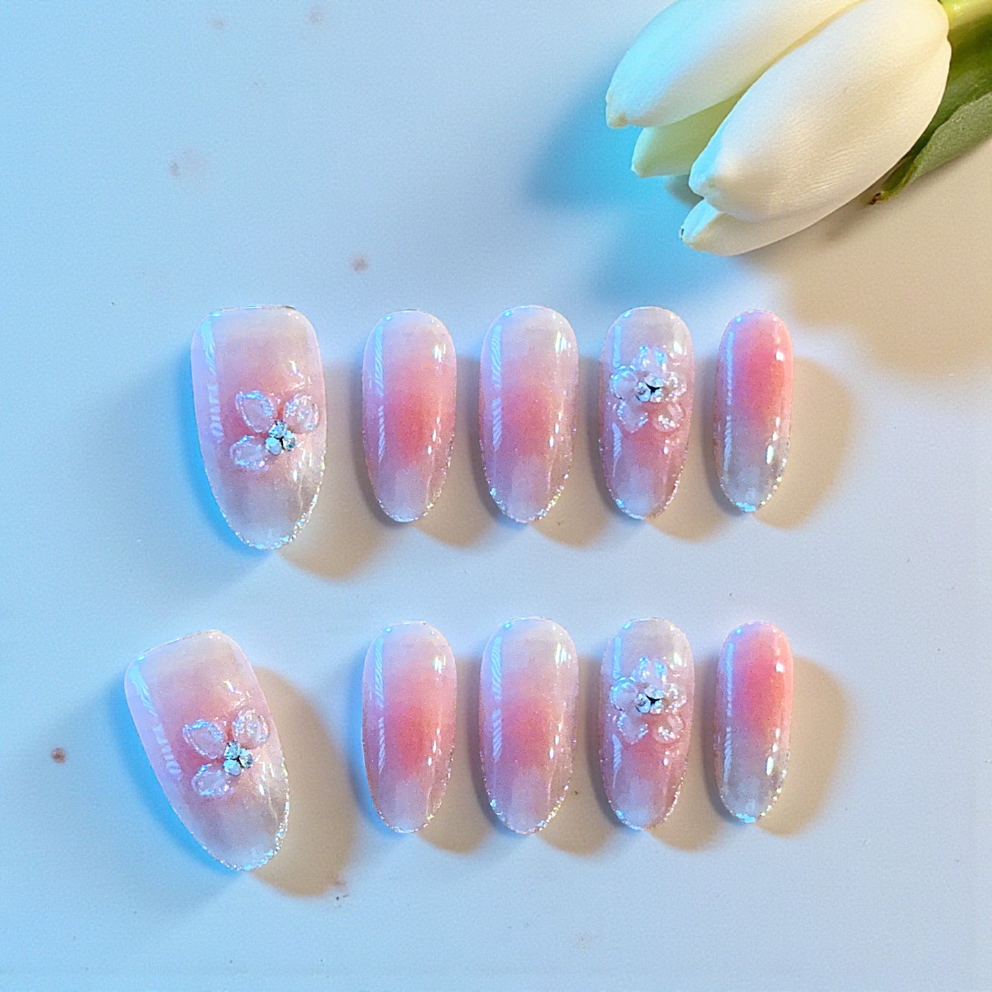 Set of pink and purple gradient nails with floral designs on a light background.