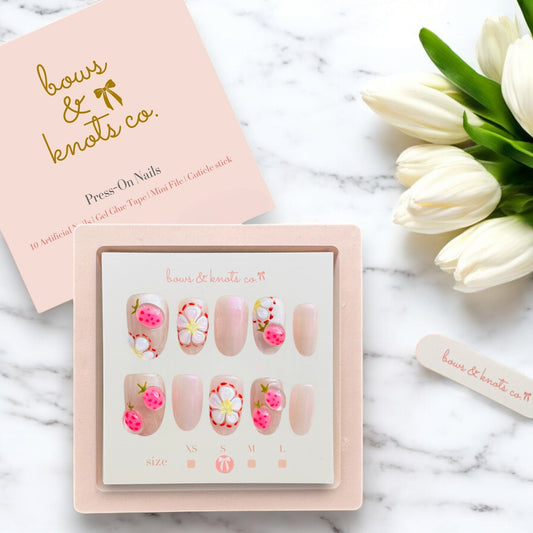Set of press-on nails with floral designs in a box, accompanied by a small bouquet of white tulips on a marble surface.