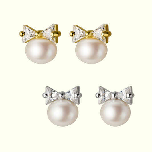 Pair of pearl earrings with bow and crystal details on a white background