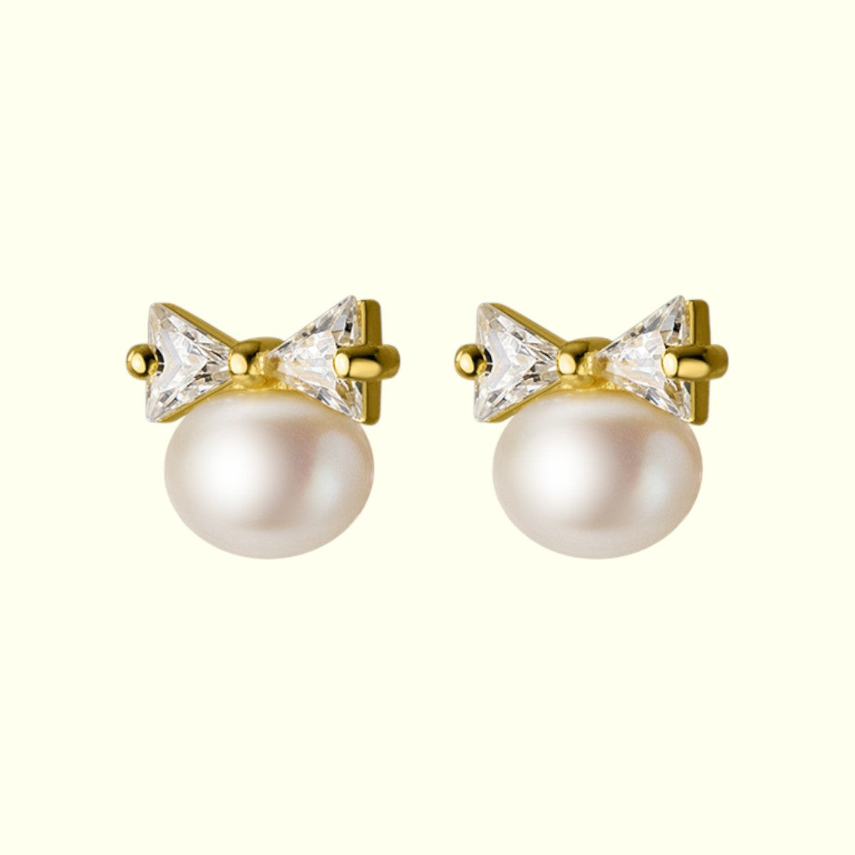 Pair of pearl earrings with gold bow and crystal accents on a white background