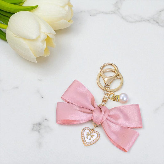 Pink bow keychain with heart charm on a marble surface with white tulips.