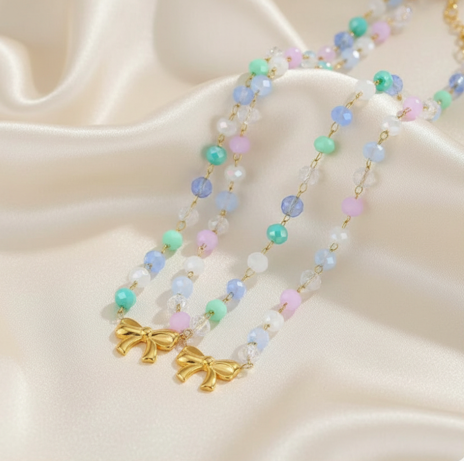 Necklace with pastel beads and gold bow charms on a beige fabric background