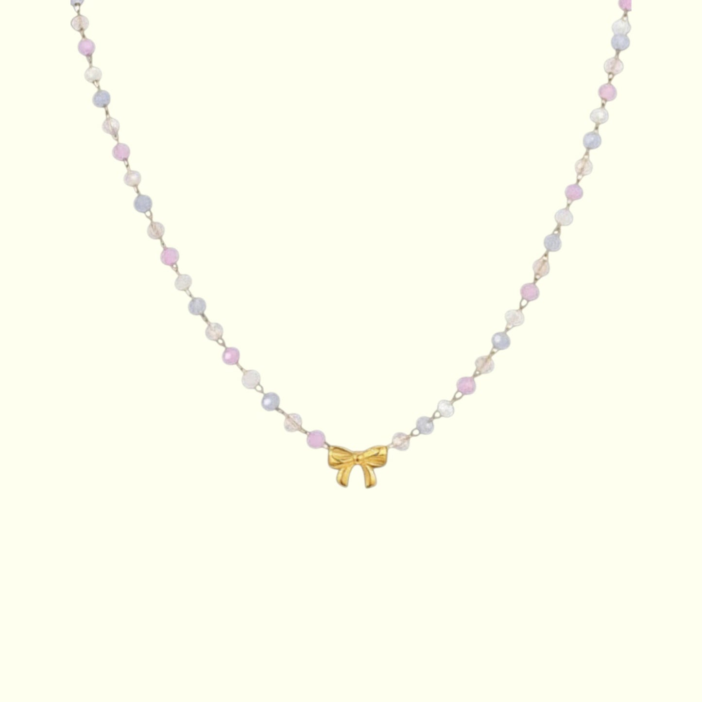 Necklace with pastel bead chain and gold bow pendant on a white background