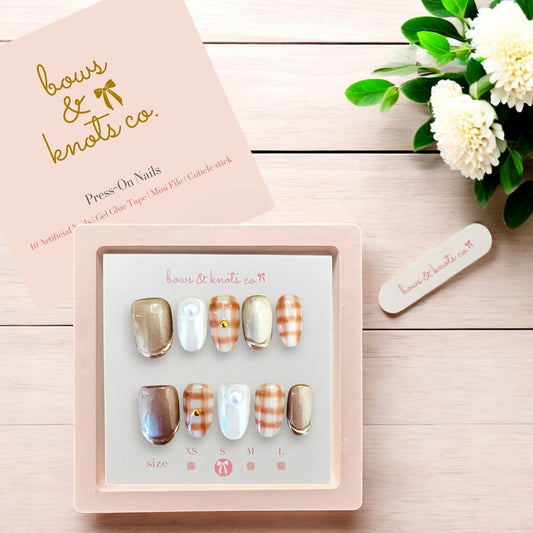 Set of press-on nails in various designs with a pink box labeled 'bows & knots co.' on a wooden surface.