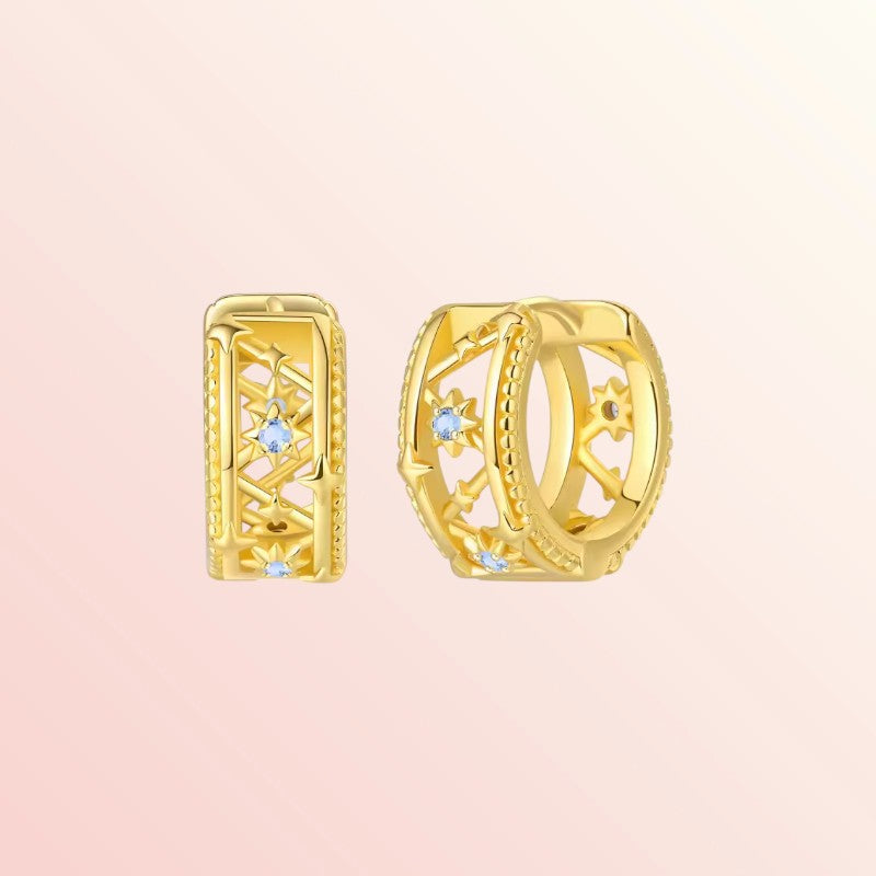 Gold hoop earrings with gemstones on a light pink background