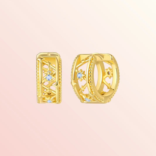Gold hoop earrings with gemstones on a light pink background