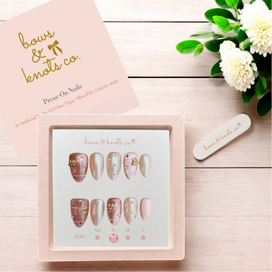 Set of press-on nails with a display box, pink packaging, and flowers on a wooden surface.
