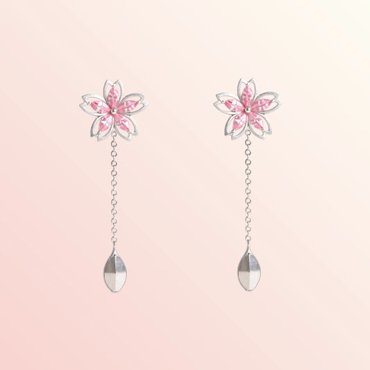 Flower-shaped earrings with pink petals and clear droplets on a light pink background