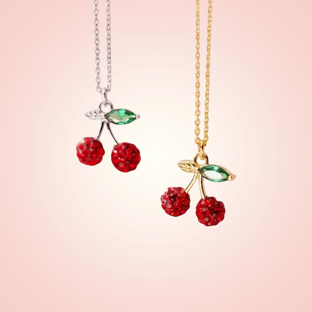 Two cherry-themed necklaces on a pink background
