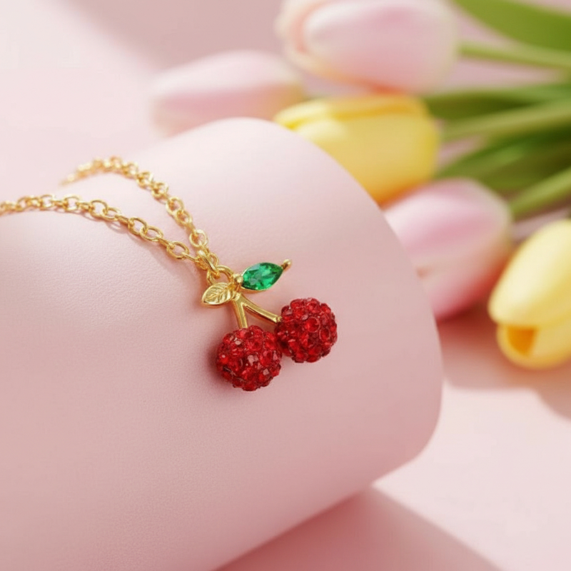 Gold necklace with red berry pendants on a pink surface with tulips in the background