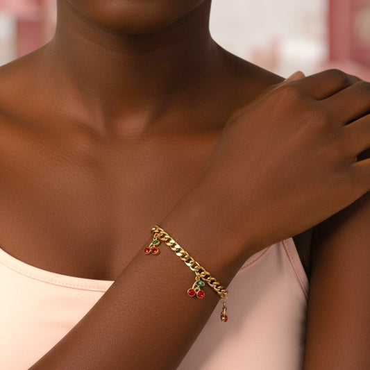 Gold bracelet with red and green beads on a person's wrist against a blurred background