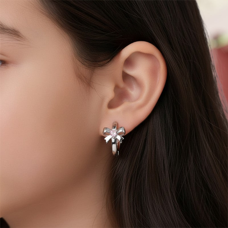 Close-up of an ear wearing a silver bowknot-shaped earring with a blurred background