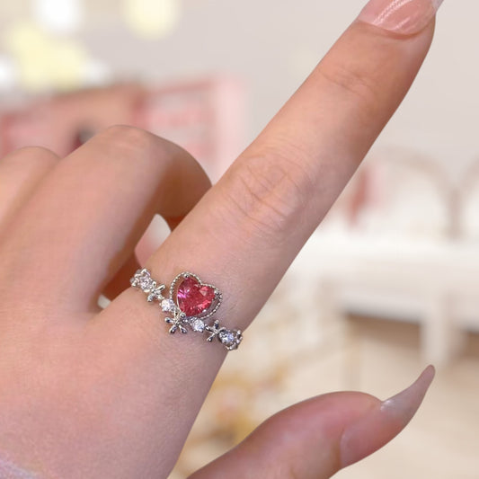 Heart-shaped pink gemstone ring on a finger with a blurred background