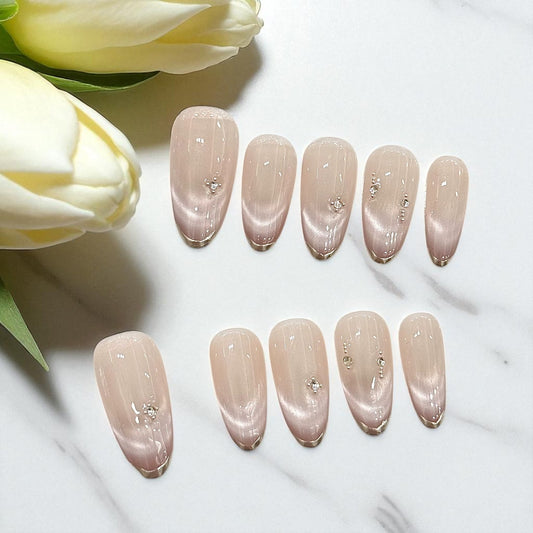 Set of nude-colored nail polish samples with decorative crystals on a white surface with tulips.