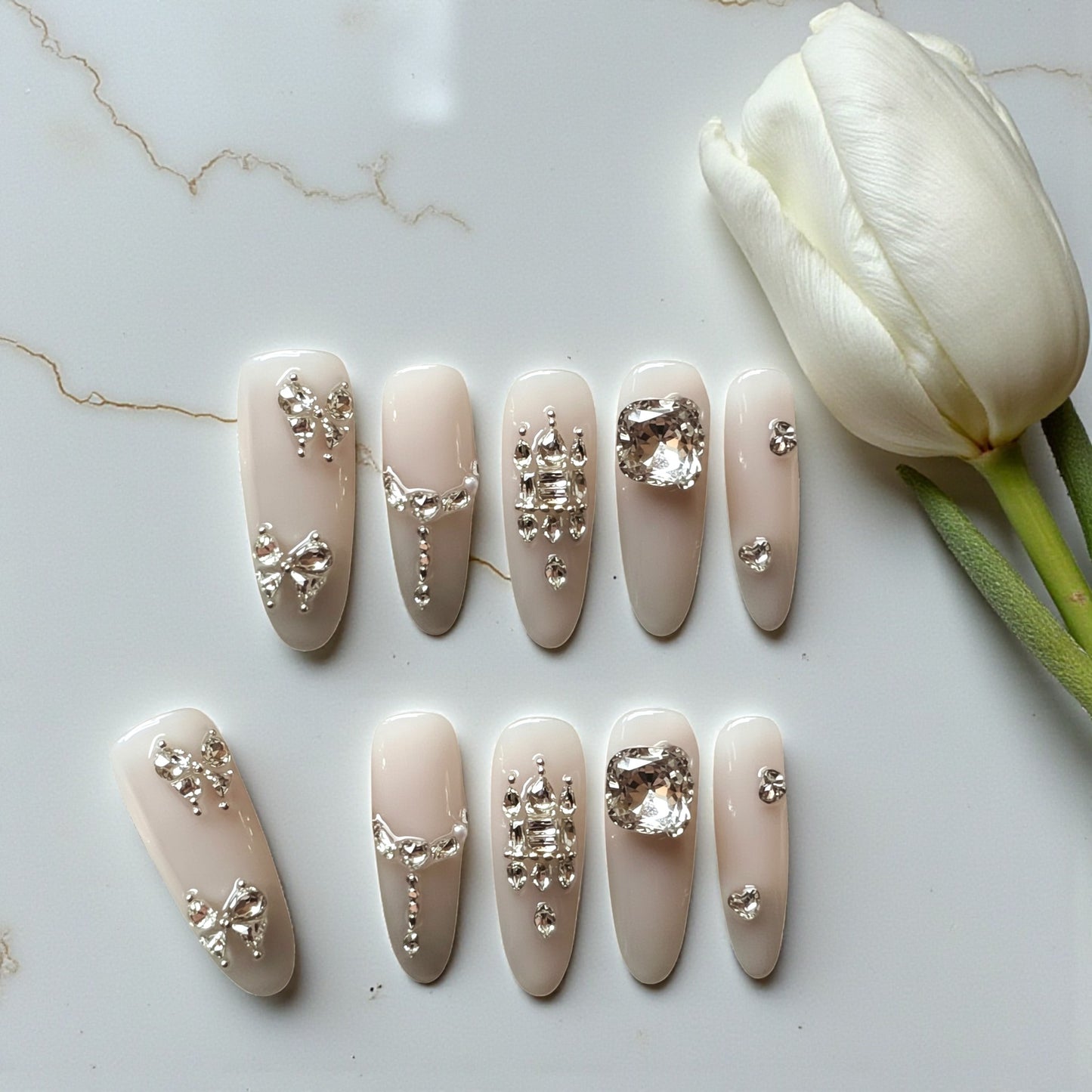 Decorative beige nail art with crystals on a marble surface with a white tulip.