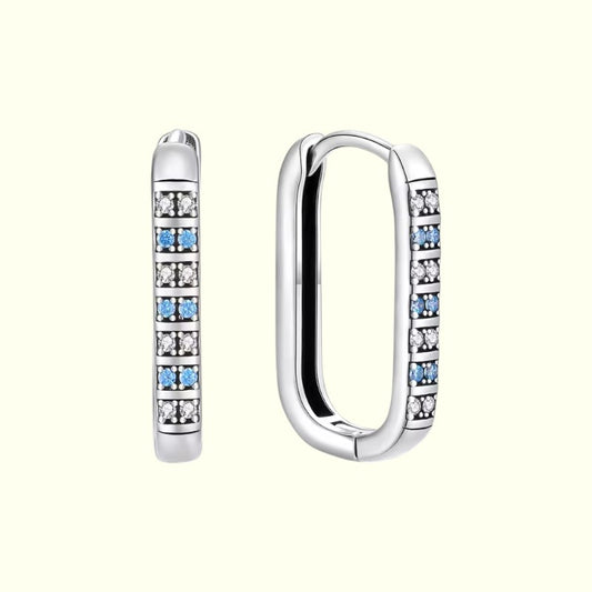 Silver hoop earrings with embedded blue and clear gemstones on a white background