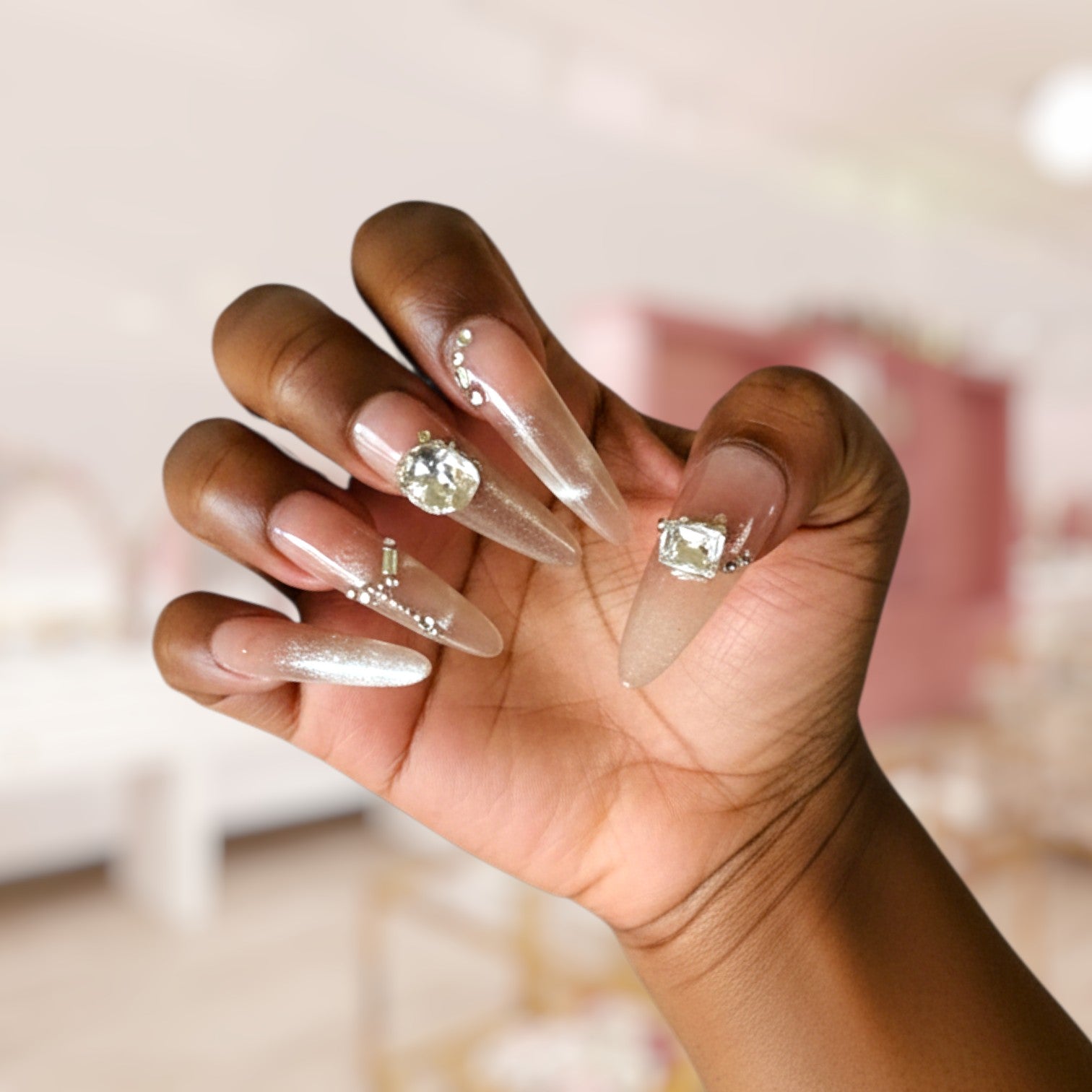 Hand with long, decorative nails featuring gemstones against a blurred background