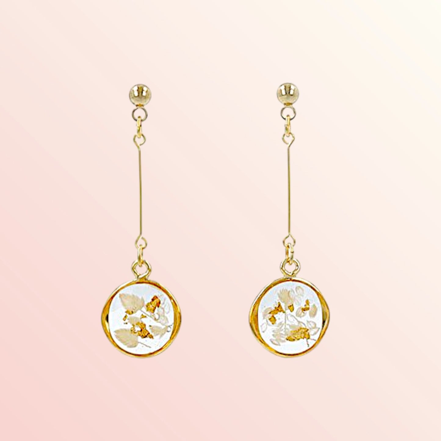 Pair of gold earrings with floral designs on a pink background