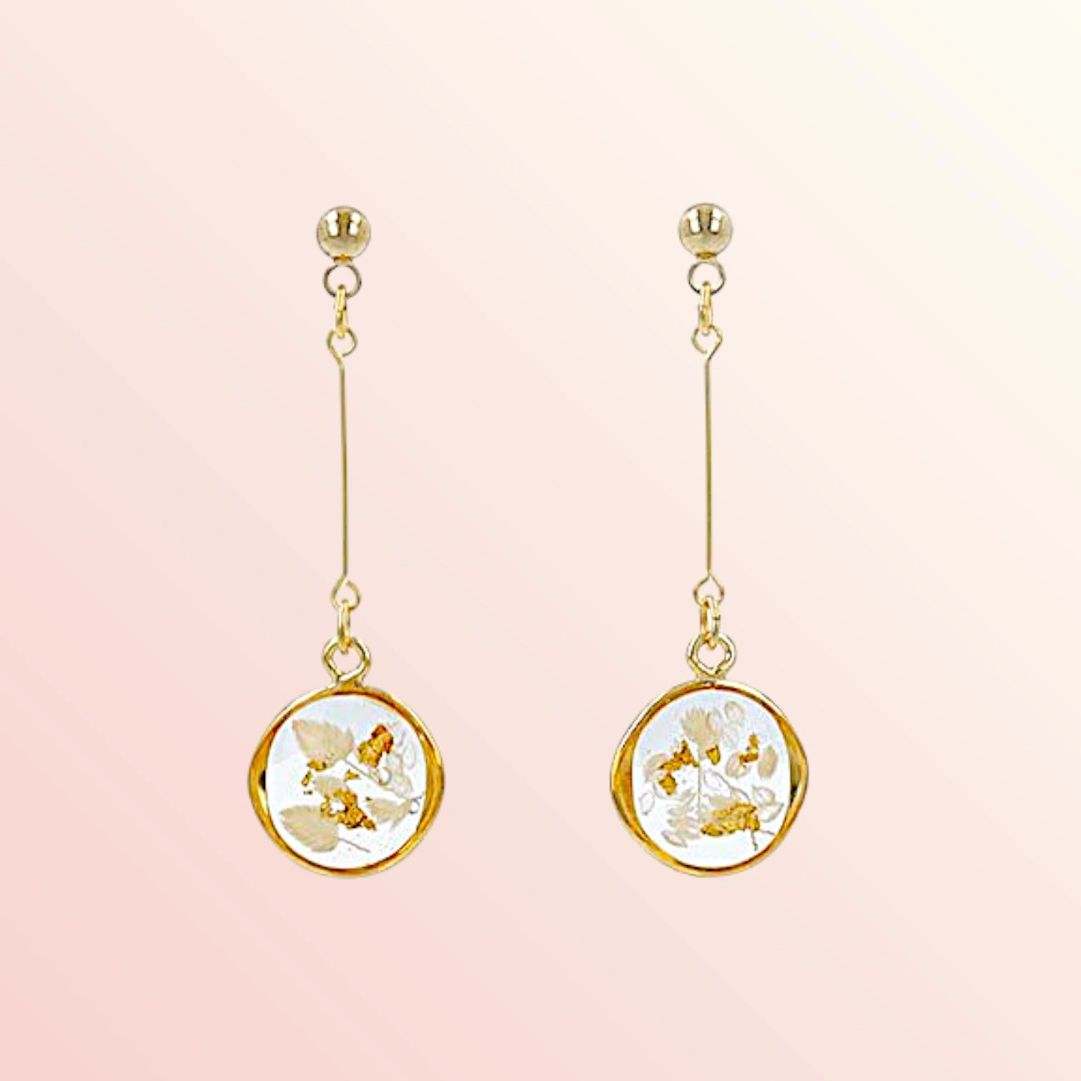 Pair of gold earrings with floral designs on a pink background