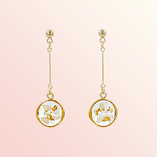 Pair of gold earrings with floral designs on a pink background