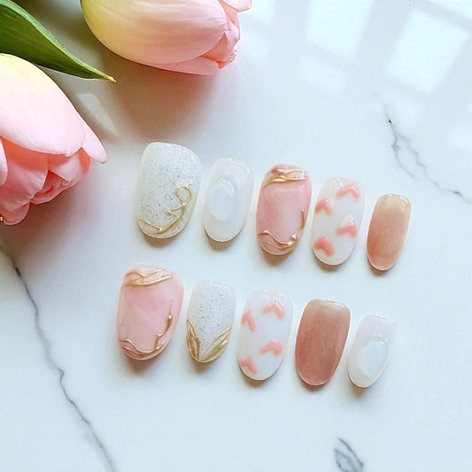Set of nail art samples with pink and gold designs on a marble surface with flowers.