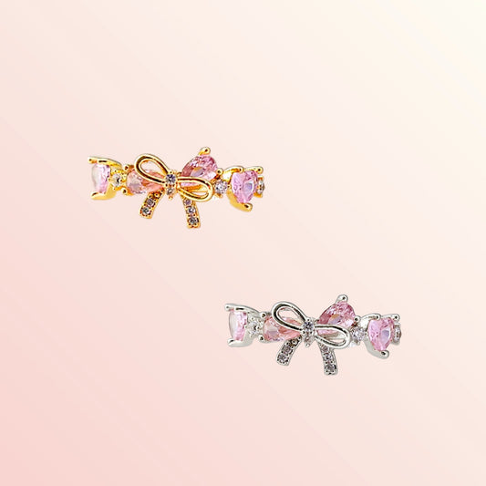 Two bow-shaped earrings with pink gemstones on a light pink background