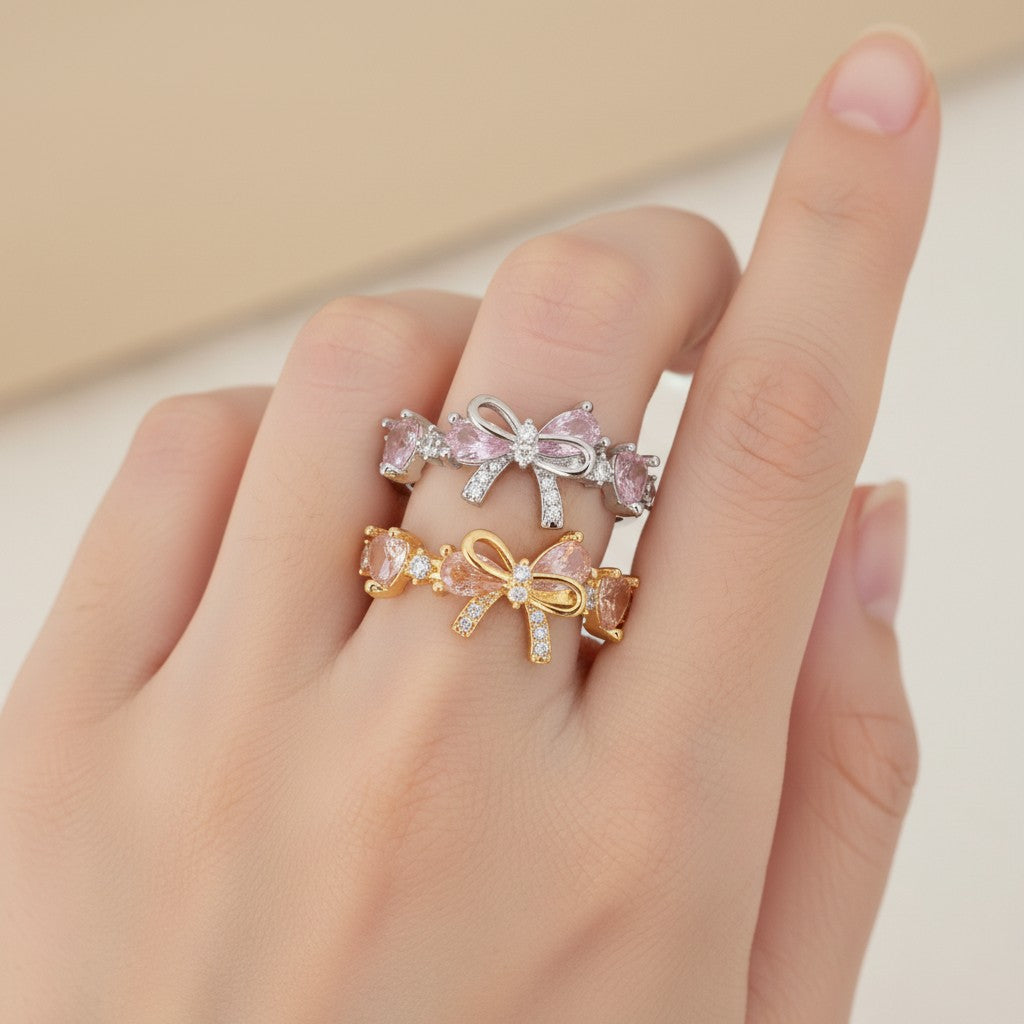 Three bow-shaped rings in gold, silver, and rose gold on a hand against a neutral background