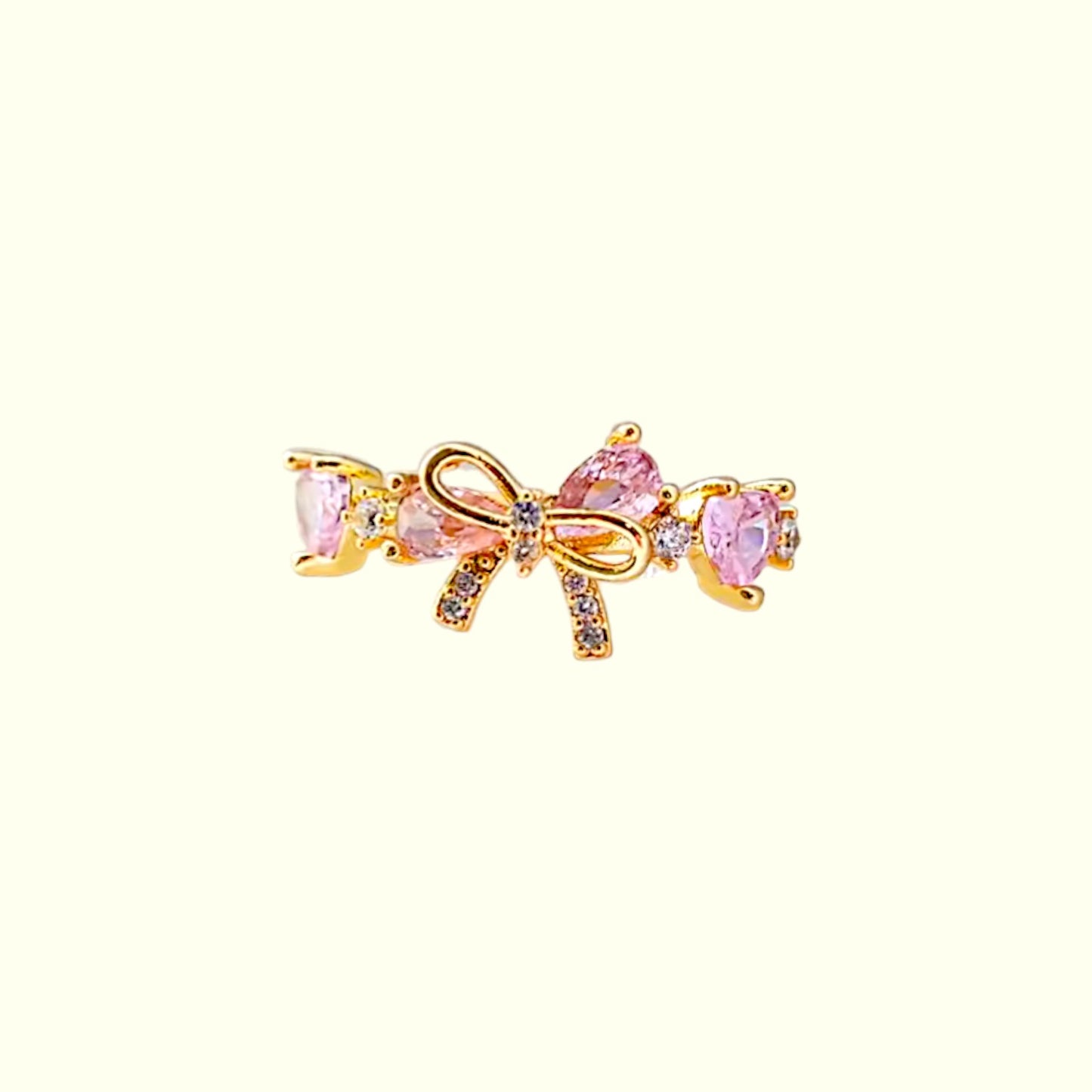 Gold bow-shaped earring with pink gemstones on a white background
