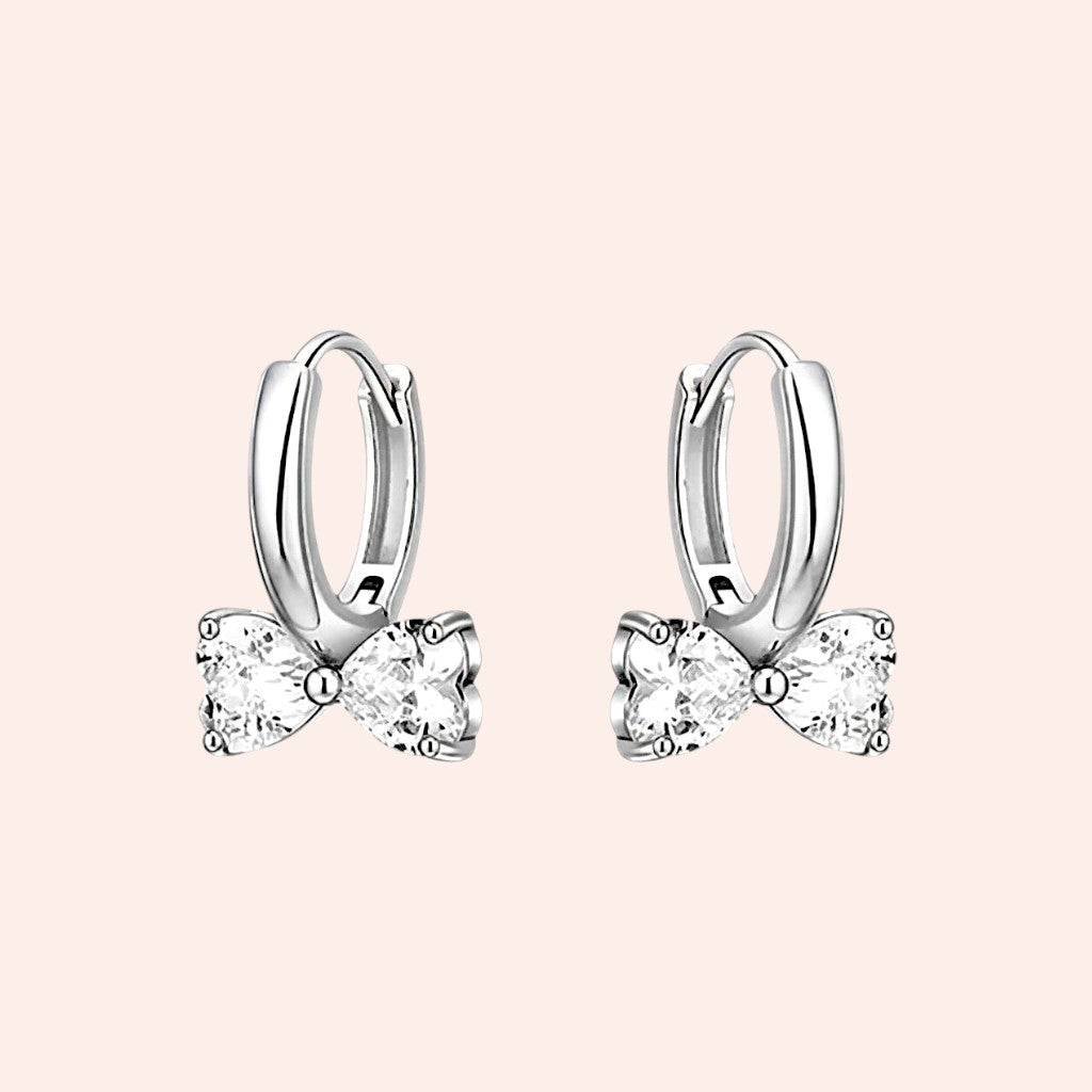Silver hoop earrings with bow designs on a light pink background