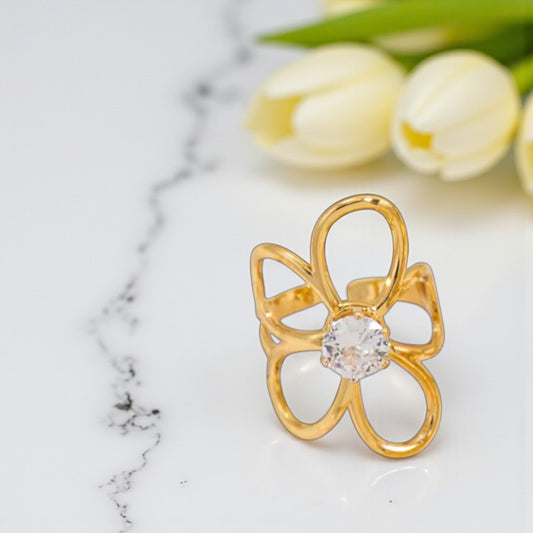 Gold flower ring with a clear gemstone on a marble surface with white tulips in the background.