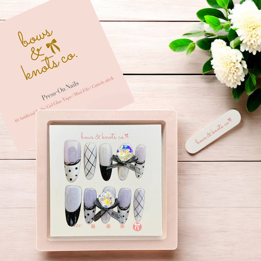 Box of press-on nails with a pink cover and floral arrangement on a wooden surface