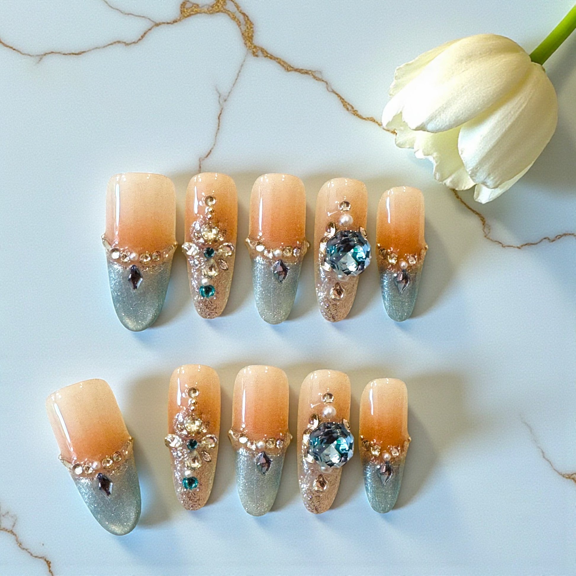 Decorative nails with gemstones on a marble surface with a tulip.