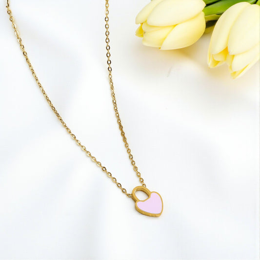 Gold necklace with a pink heart pendant on a white background with yellow tulips.