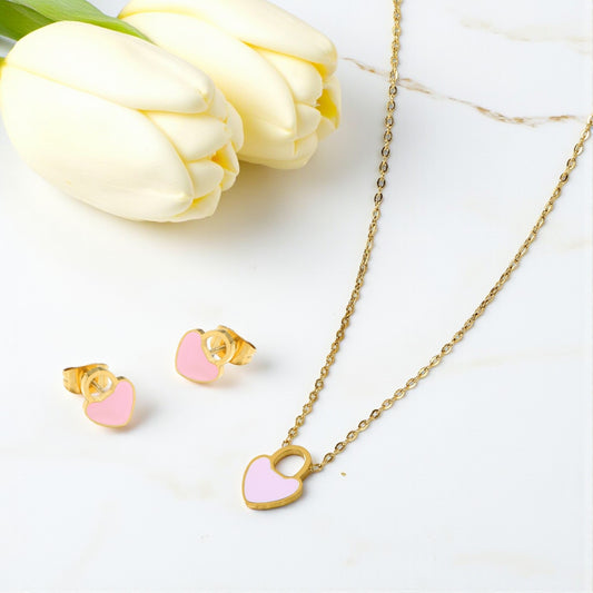 Gold necklace with pink heart pendant and matching earrings on a white surface with tulips.